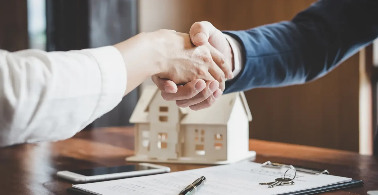Une agente immobilière présente une maison en briques à un couple d'acheteurs dans une rue résidentielle d'Elbeuf.
