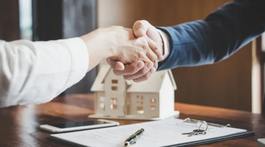 Une agente immobilière présente une maison en briques à un couple d'acheteurs dans une rue résidentielle d'Elbeuf.